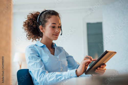 Smiling customer service representative using tablet PC sitting at desk in office photo