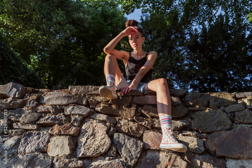 Non-binary hipster sitting on stone wall