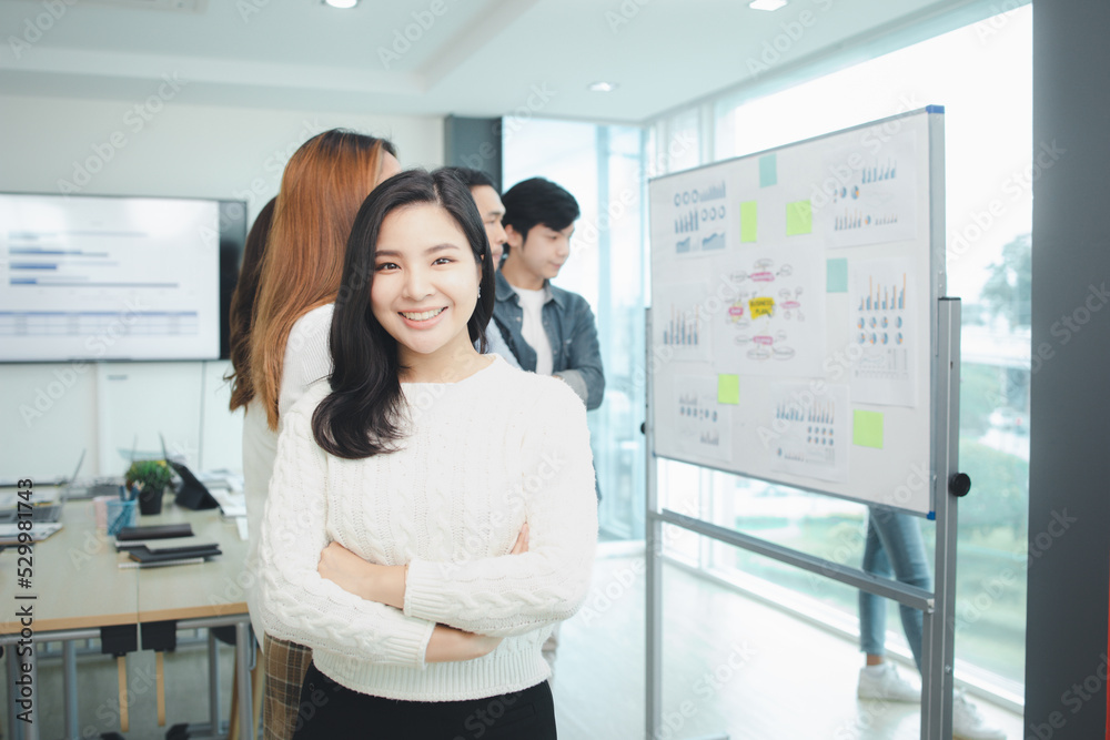 An Asian woman with her arms crossed in a startup company meeting room, she is a company employee of the international marketing department, she attends a company meeting. An Asian woman with her arms crossed in a startup company meeting room, she is a company employee of the international marketing department, she attends a company meeting.