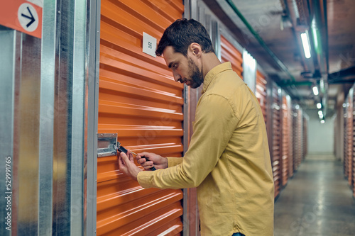 Fotografie Concentrated young man padlocking the storage unit door
