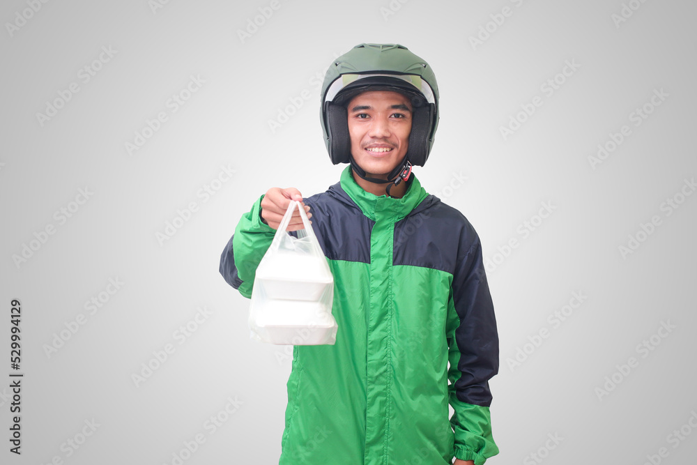 Portrait of Asian online taxi driver wearing green jacket and helmet holding food wrapped in foam plastic box. Isolated image on white background Portrait of Asian online taxi driver wearing green jacket and helmet holding food wrapped in foam plastic box. Isolated image on white background