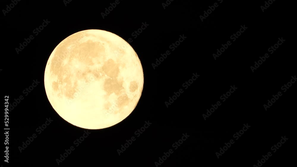 A glowing golden huge full moon seen from earth through the atmosphere against a starry night sky. A large full moon moves across the sky, the moon moving from the left frame to the right. A glowing golden huge full moon seen from earth through the atmosphere against a starry night sky. A large full moon moves across the sky, the moon moving from the left frame to the right.