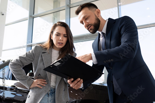 Billede på lærred displeased young woman in car dealership arguing with car dealer