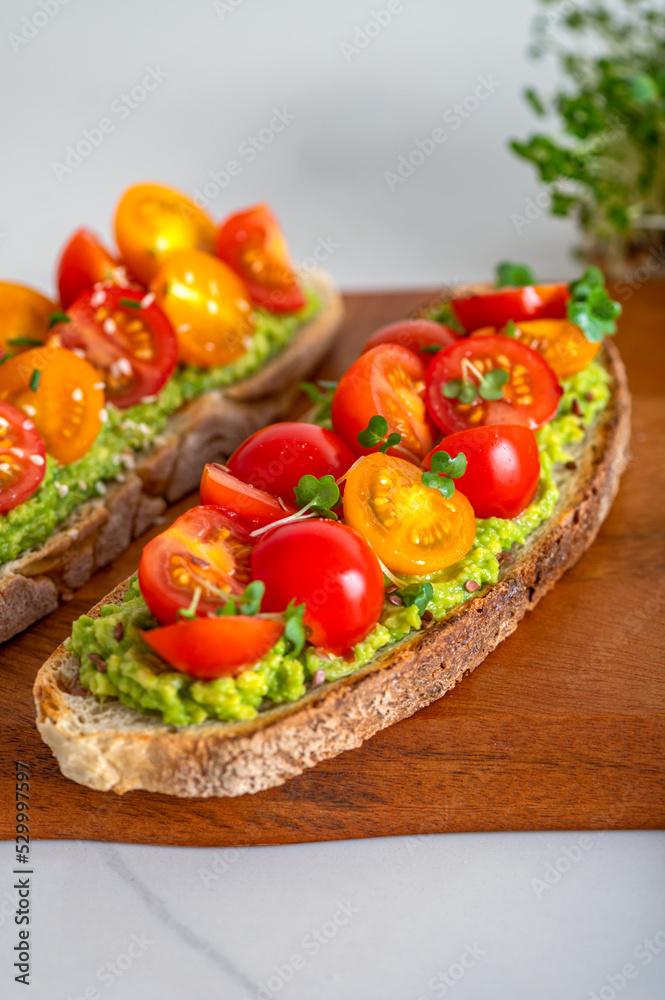 Tasty open sandwich from toasted sourdough bread with mashed avocado and fresh tomatoes