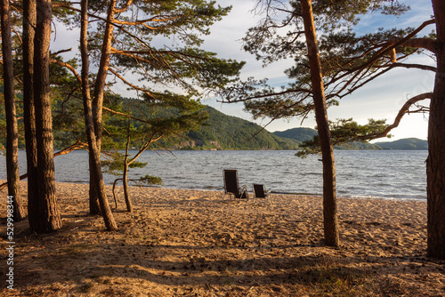 Concept parent chair and child chair on sand beach sunset with sea, pine trees and mauntain on background
