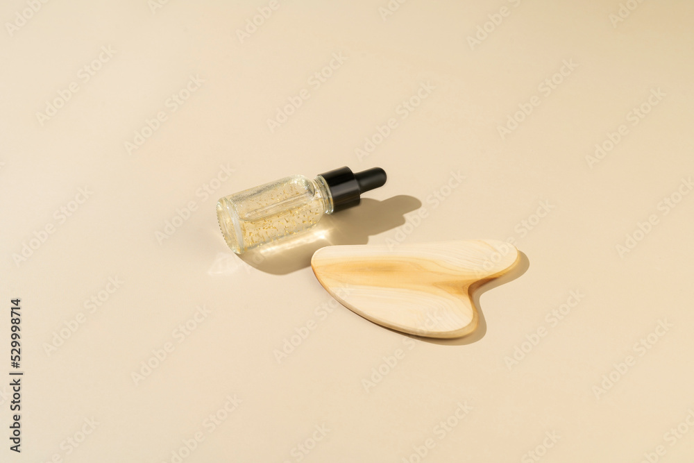 A wooden face massager and an antiaging serum with golden parts lying on a beige background A wooden face massager and an antiaging serum with golden parts lying on a beige background
