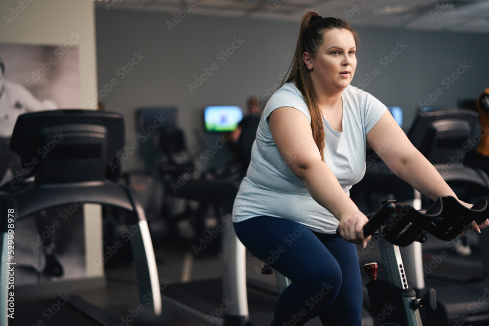 Overweight caucasian woman riding a bike at the gym