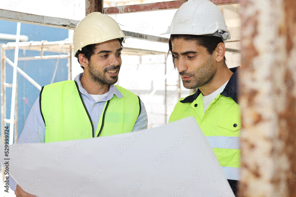 Two technician civil engineer or specialist inspector discussing, brainstorm and planing work with laptop, blueprint and walkie talkie radio together at Industrial building site. Construction concept