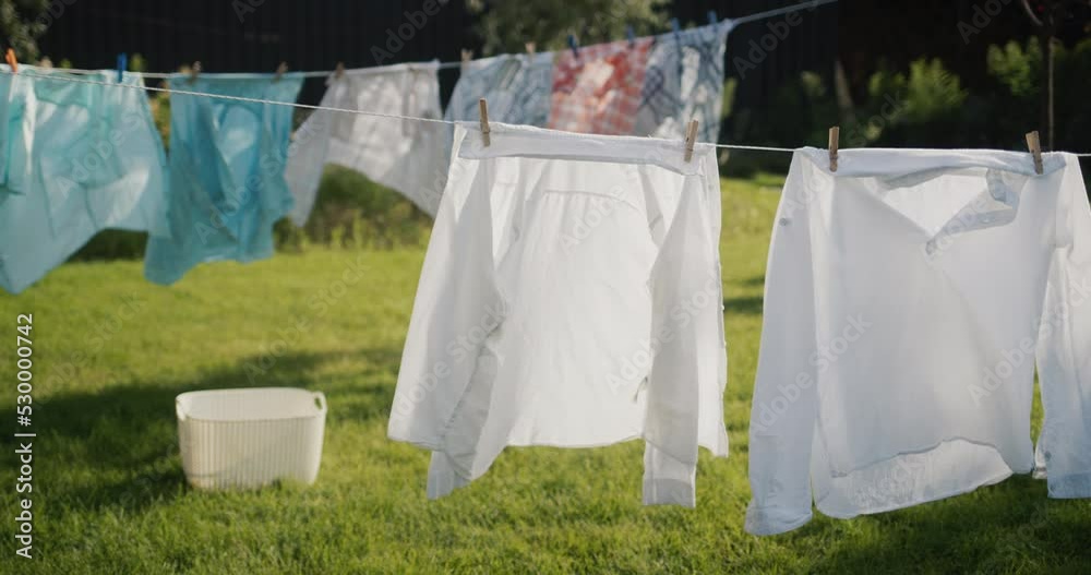 Clothes and bedding are drying in the backyard of the house, a laundry basket is standing on the grass nearby.