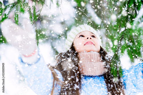 A Joyful little girl is raising her palms to the fir-tree branches.