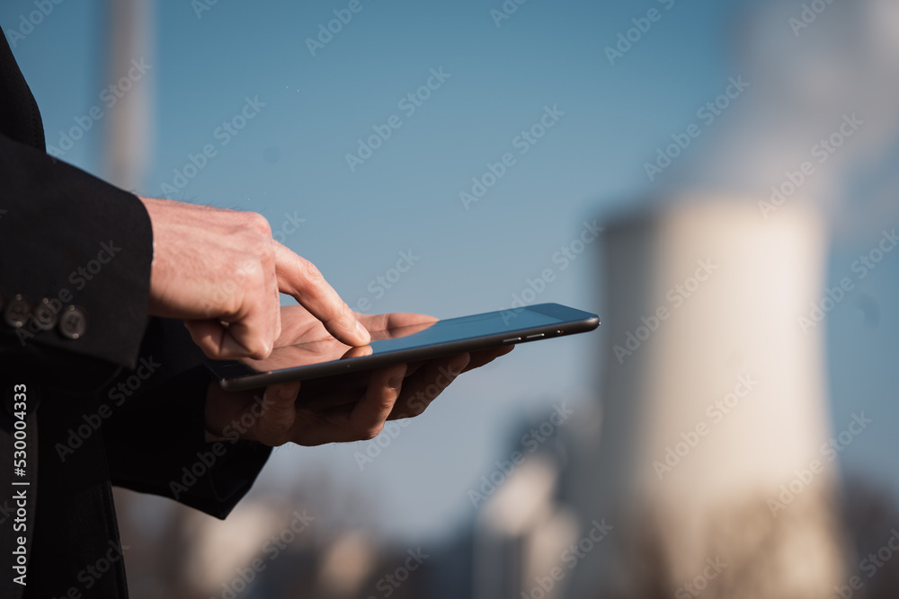 Close up of tablet electric engineer at coal fired power station in background at energy crisis Close up of tablet electric engineer at coal fired power station in background at energy crisis
