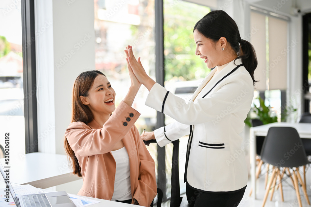 Obraz premium Asian businesswomen are laughing and celebrating their success together, giving high-fives