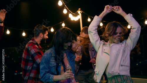 On the rooftop of terrace group of friends have fun time dancing and feeling happy at the party night time they drinking champagne