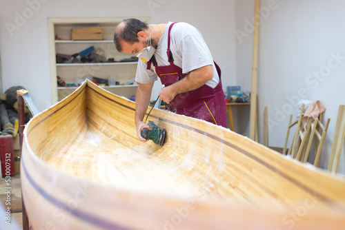 Young carpenter making wooden boat in his carpentry workshop 