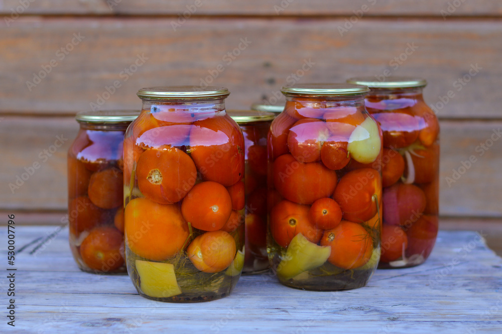Some glass jars with canned tomatoes with iron lids stand on a wooden table. home storage solution, saving leftovers, canning concept, rustic composition Some glass jars with canned tomatoes with iron lids stand on a wooden table. home storage solution, saving leftovers, canning concept, rustic composition
