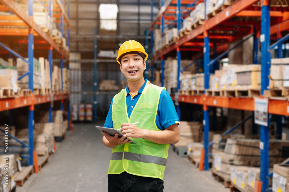 Male factory manager using digital tablet in warehouse shelf looking at camera.Products and corrugated cardboard.looking at camera Male factory manager using digital tablet in warehouse shelf looking at camera.Products and corrugated cardboard.looking at camera