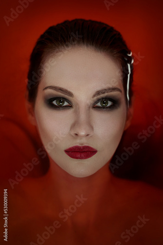 Portrait of a gothic vampire girl with pale skin in bloody water.