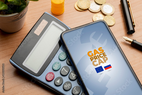 Gas price cap concept: smartphone over a calculator on a wooden table sorrounded by some euro coins photo