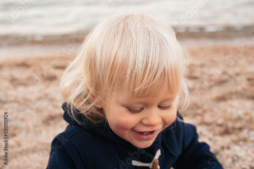 portrait of smiling baby boy sitting on sand on beach in autumn time © Marharyta