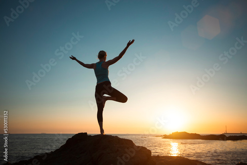 A woman does yoga  meditating near the ocean. A silhouette in the sunset.