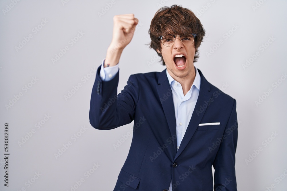 Hispanic business young man wearing glasses angry and mad raising fist frustrated and furious while shouting with anger. rage and aggressive concept. Hispanic business young man wearing glasses angry and mad raising fist frustrated and furious while shouting with anger. rage and aggressive concept.