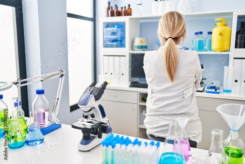 Middle age blonde woman working at scientist laboratory standing backwards looking away with crossed arms
