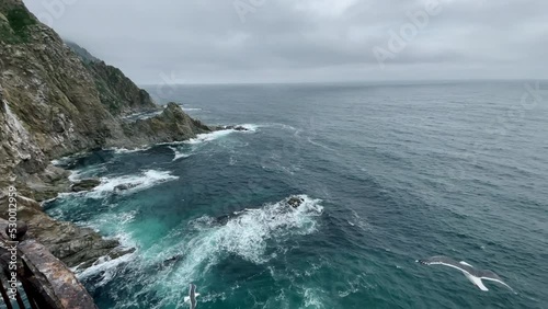 Panorama from observation deck of Aniva lighthouse to majestic Sakhalin Island, ocean waves crashing on rocks of Cape Aniva and soaring seagulls  photo