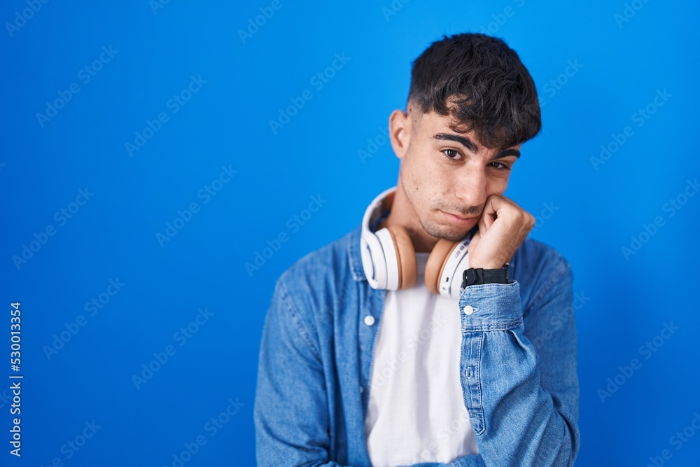 Young hispanic man standing over blue background thinking looking tired and bored with depression problems with crossed arms. Young hispanic man standing over blue background thinking looking tired and bored with depression problems with crossed arms.