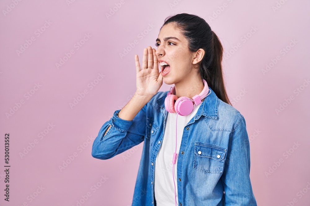 Young beautiful woman standing over pink background shouting and screaming loud to side with hand on mouth. communication concept. Young beautiful woman standing over pink background shouting and screaming loud to side with hand on mouth. communication concept.