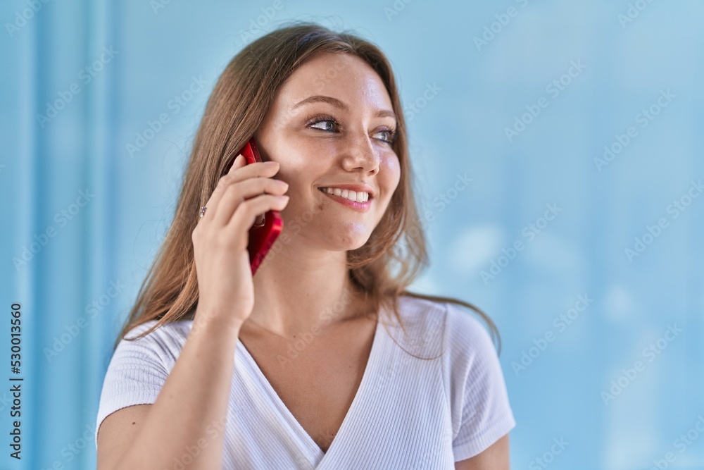 Young blonde woman smiling confident talking on the smartphone over isolated blue wall background Young blonde woman smiling confident talking on the smartphone over isolated blue wall background