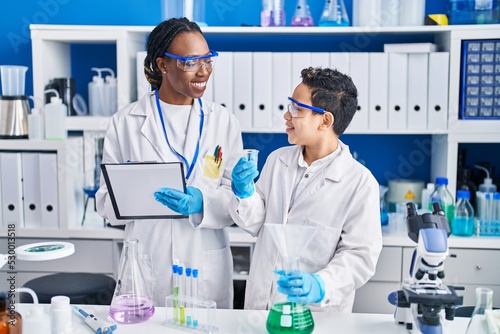 African american mother and son scientists smiling confident measuring liquid laboratory