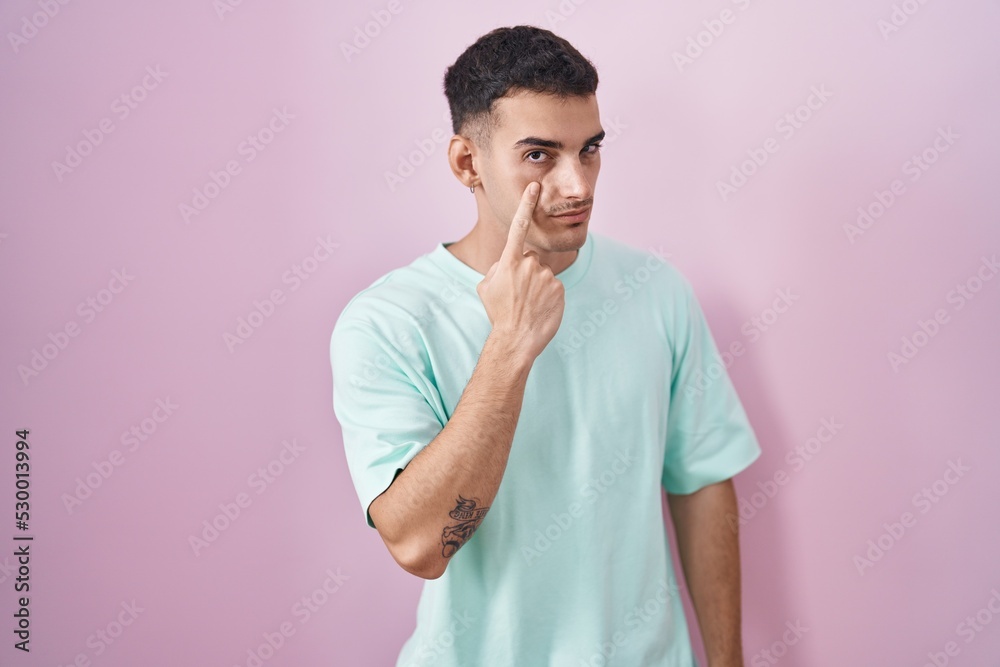 Handsome hispanic man standing over pink background pointing to the eye watching you gesture, suspicious expression Handsome hispanic man standing over pink background pointing to the eye watching you gesture, suspicious expression