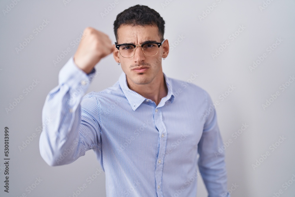Handsome hispanic man wearing business clothes and glasses angry and mad raising fist frustrated and furious while shouting with anger. rage and aggressive concept. Handsome hispanic man wearing business clothes and glasses angry and mad raising fist frustrated and furious while shouting with anger. rage and aggressive concept.