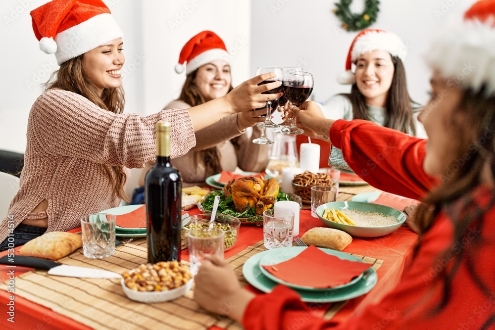 Group of young hispanic women smiling happy having christmas dinner and toasting with wine at home.
