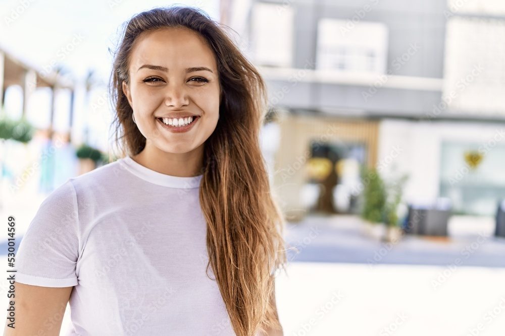 Attractive and beautiful hispanic woman smiling happy on a sunny day outdoors. Pretty brunette girl with positive smile looking confident at the city