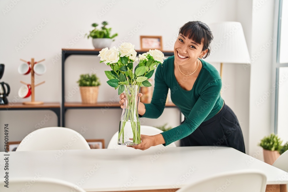 Young beautiful hispanic woman smiling confident putting plant pot on table at home