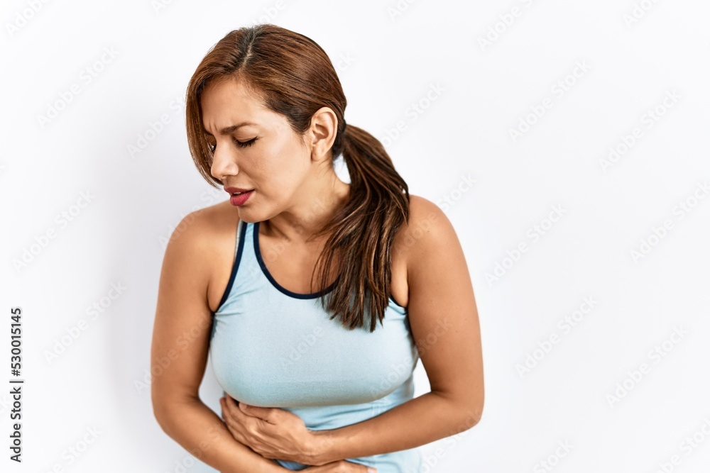 Young latin woman wearing sporty clothes over isolated background with hand on stomach because nausea, painful disease feeling unwell. ache concept. Young latin woman wearing sporty clothes over isolated background with hand on stomach because nausea, painful disease feeling unwell. ache concept.