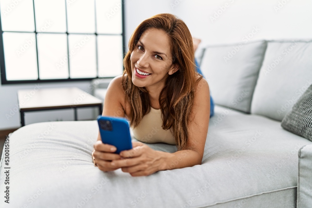 Young latin woman using smartphone lying on sofa at home Young latin woman using smartphone lying on sofa at home