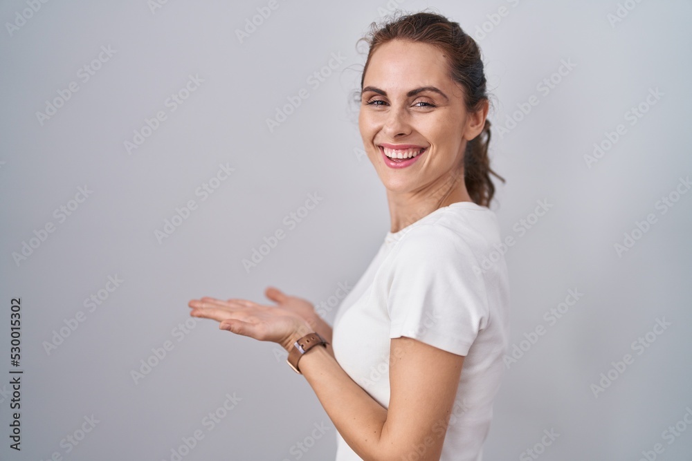 Beautiful brunette woman standing over isolated background pointing aside with hands open palms showing copy space, presenting advertisement smiling excited happy