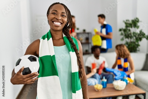 Fototapeta Naklejka Na Ścianę i Meble -  Young soccer hooligan woman wearing team scarf holding football ball at home