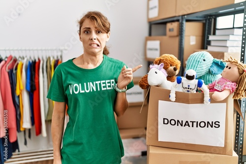 Beautiful caucasian woman wearing volunteer t shirt at donations stand pointing aside worried and nervous with forefinger, concerned and surprised expression