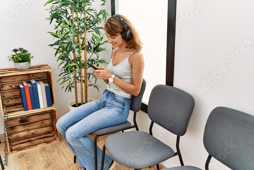 Young caucasian girl listening to music using smartphone and headphones at waiting room.