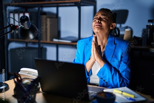 Fotografiet Beautiful african american woman working at the office at night begging and praying with hands together with hope expression on face very emotional and worried