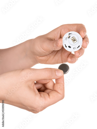 Female hands hold a miniature electronic module for a smart home, thermometer, button, remote control, etc. And a battery. Battery replacement concept. Isolated on white background