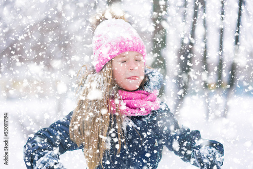 A portrait of a funny kid in pink hat during snowfall.