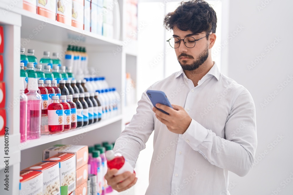 Young hispanic man client make photo to bottle by smartphone at pharmacy