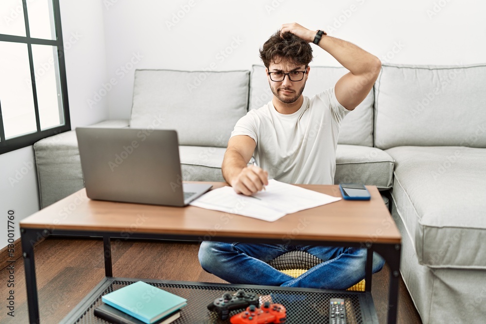 Hispanic man doing papers at home confuse and wondering about question. uncertain with doubt, thinking with hand on head. pensive concept. Hispanic man doing papers at home confuse and wondering about question. uncertain with doubt, thinking with hand on head. pensive concept.