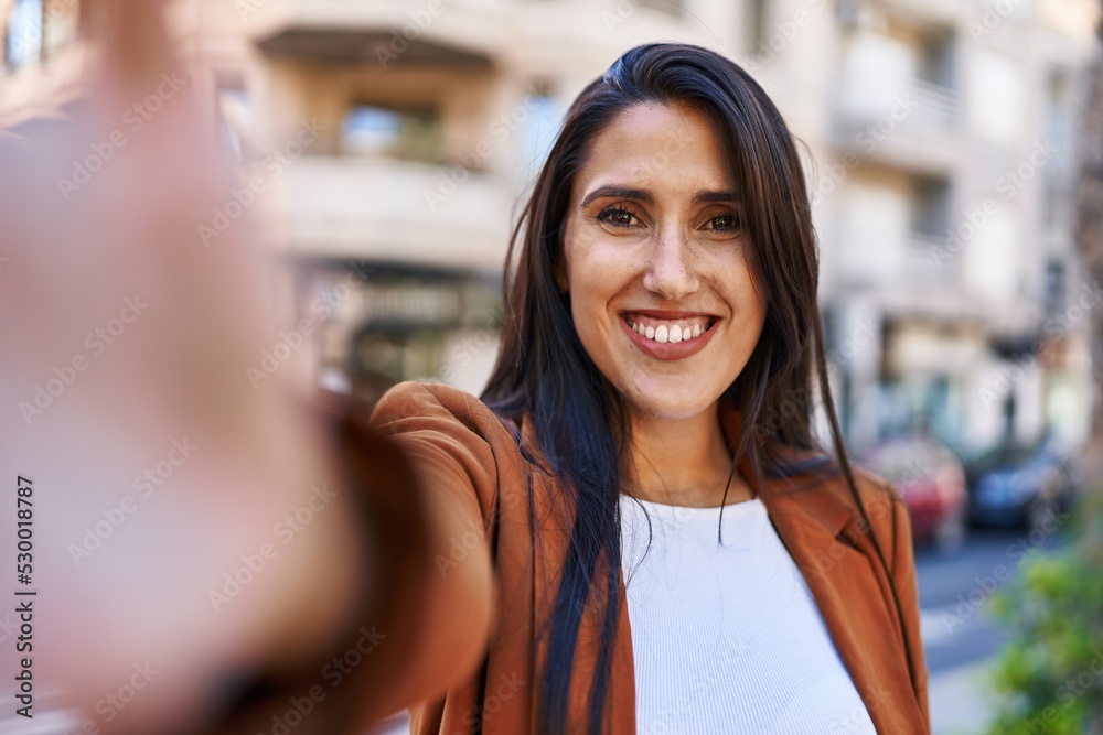 Young hispanic woman smiling confident making selfie by the camera at street