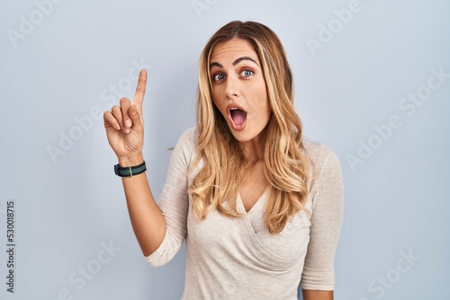 Young blonde woman standing over isolated background pointing finger up with successful idea. exited and happy. number one.