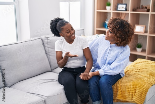 African american women mother and daughter sitting together on sofa at home